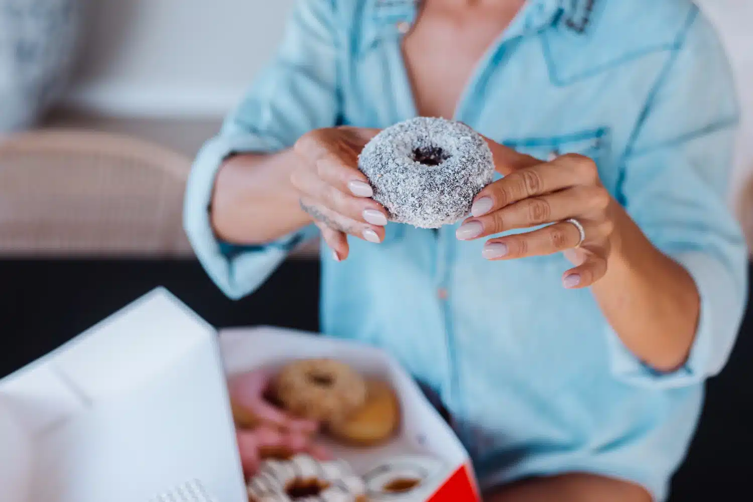personne tenant un beignet saupoudré de sucre au-dessus d’une boîte de pâtisseries